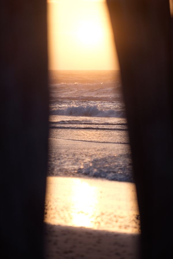 De ondergaande zon reflecteert op de zee, gekaderd door twee donkere palen.